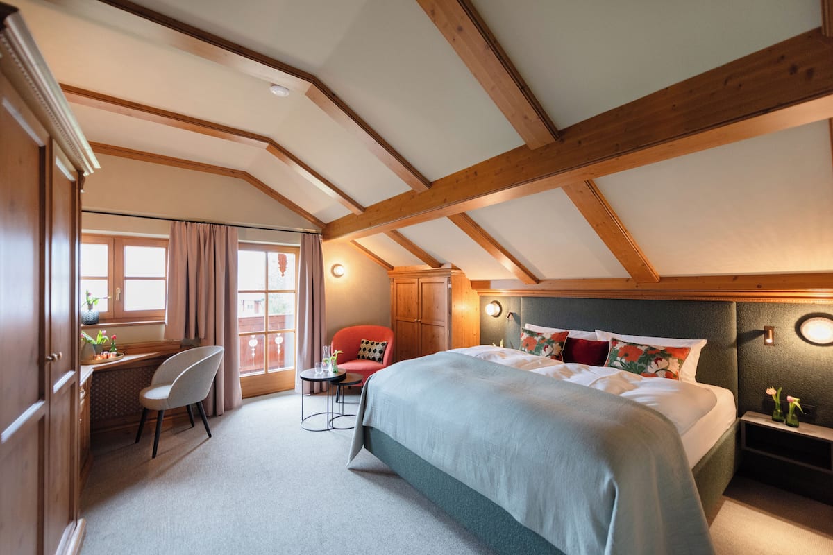A bedroom with a large bed, a desk, a chair, and a red armchair.