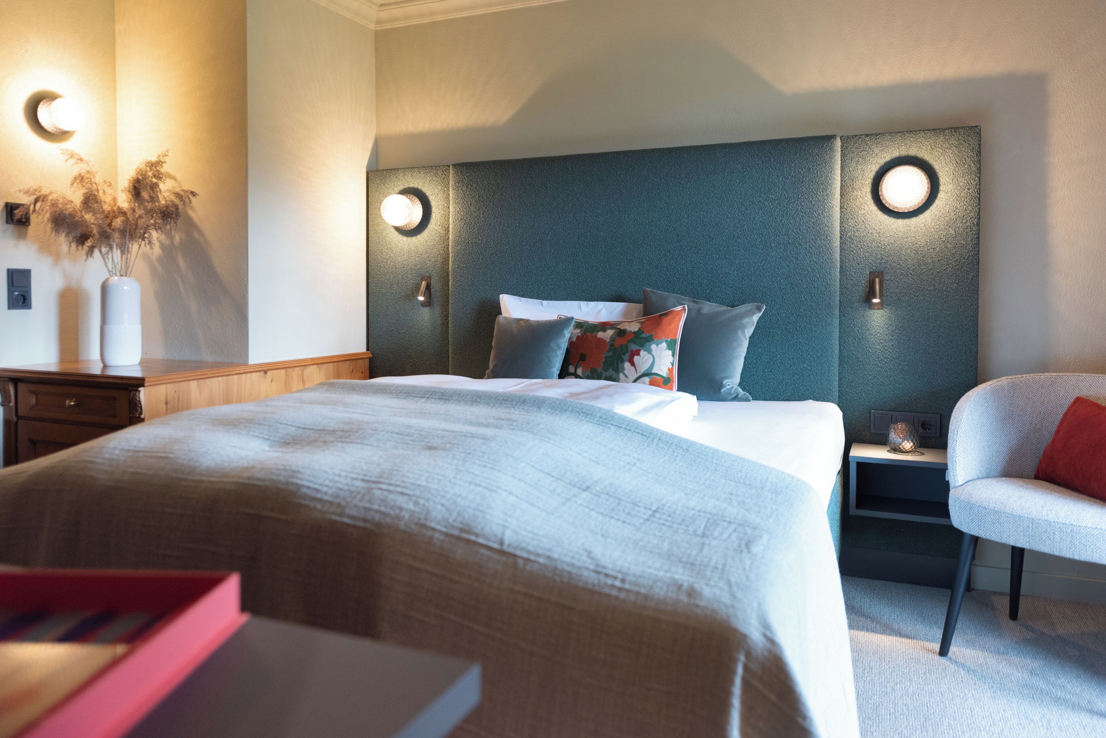A neatly arranged bedroom with a large bed, bedside tables, a chair, and wall-mounted lighting.