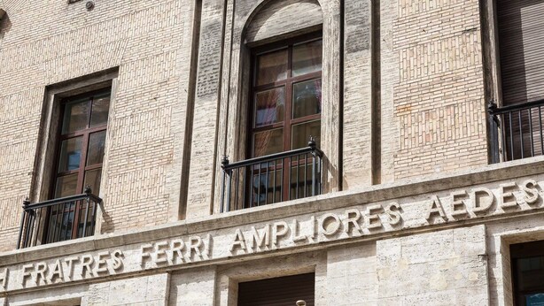 Eine Gebäudefassade mit der Aufschrift "FERRI AMPLIORS AIDES" und einem Balkon mit Metallgeländer.
