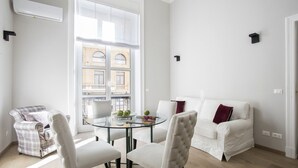 Ein modernes Wohnzimmer mit Glastisch, weißem Sofa und Sesseln mit Karomuster.