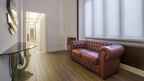 Ein modernes Wohnzimmer mit einem Glastisch, einem Ledersofa und einem großen Fenster mit Jalousien.
