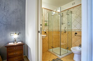 Ein Badezimmer mit einer Duschkabine aus Glas, einem Waschbecken auf Säule und einem Holzschrank mit Schubladen.