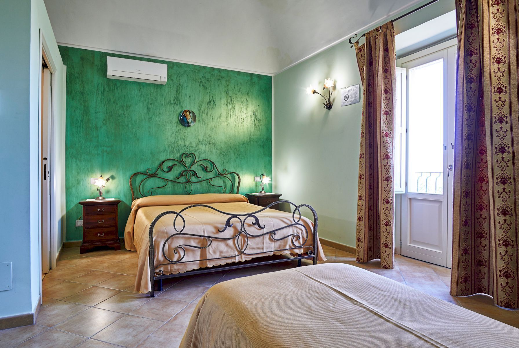 A bedroom with a green wall, a bed with a metal frame, a nightstand, and a wall-mounted light fixture.