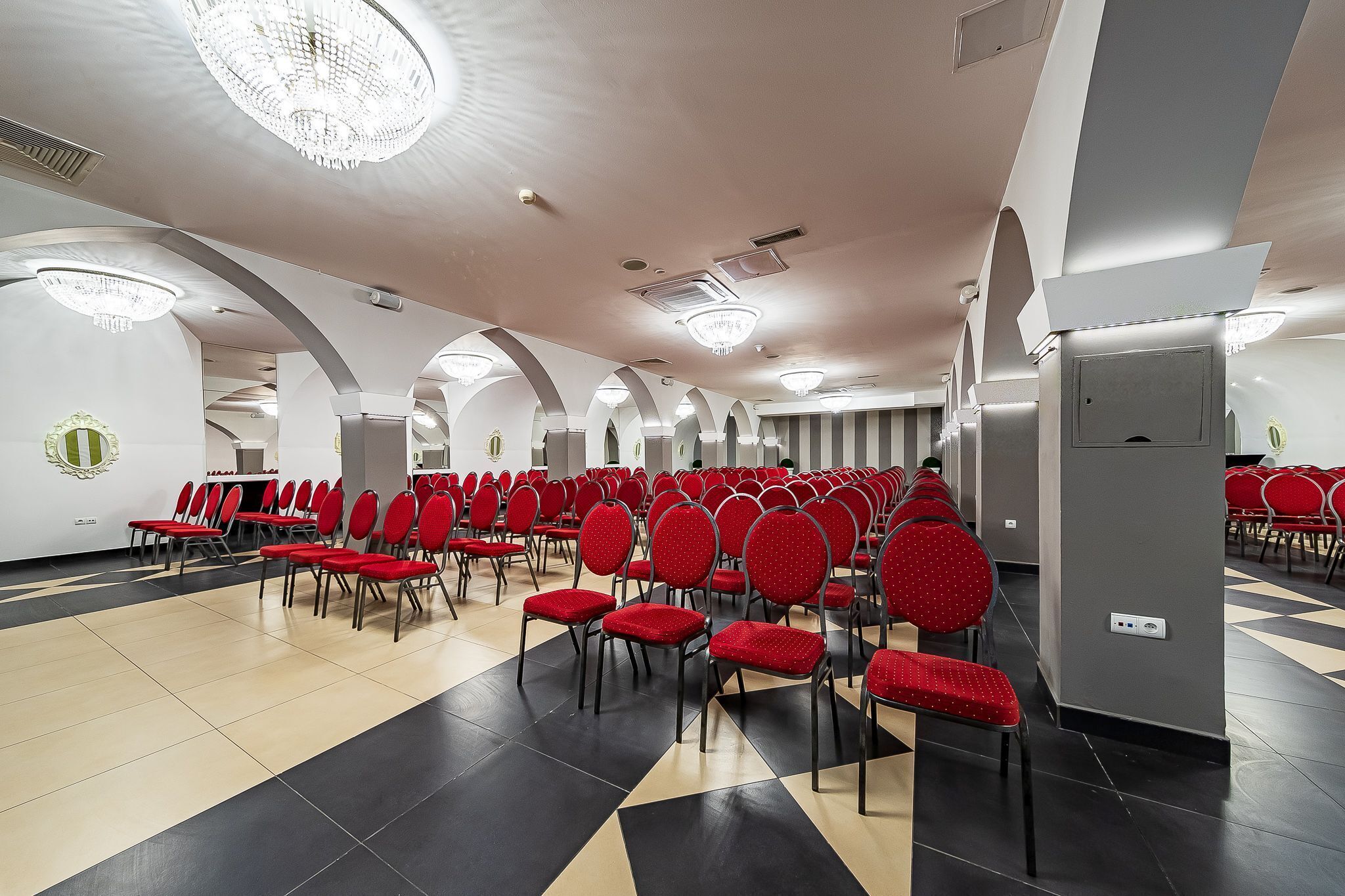 A spacious hall with rows of red chairs, a checkered floor, and a large chandelier.