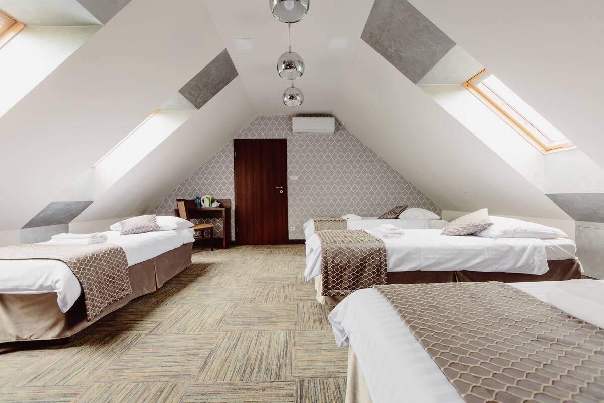 Quarto com duas camas, uma escrivaninha e um claraboia.