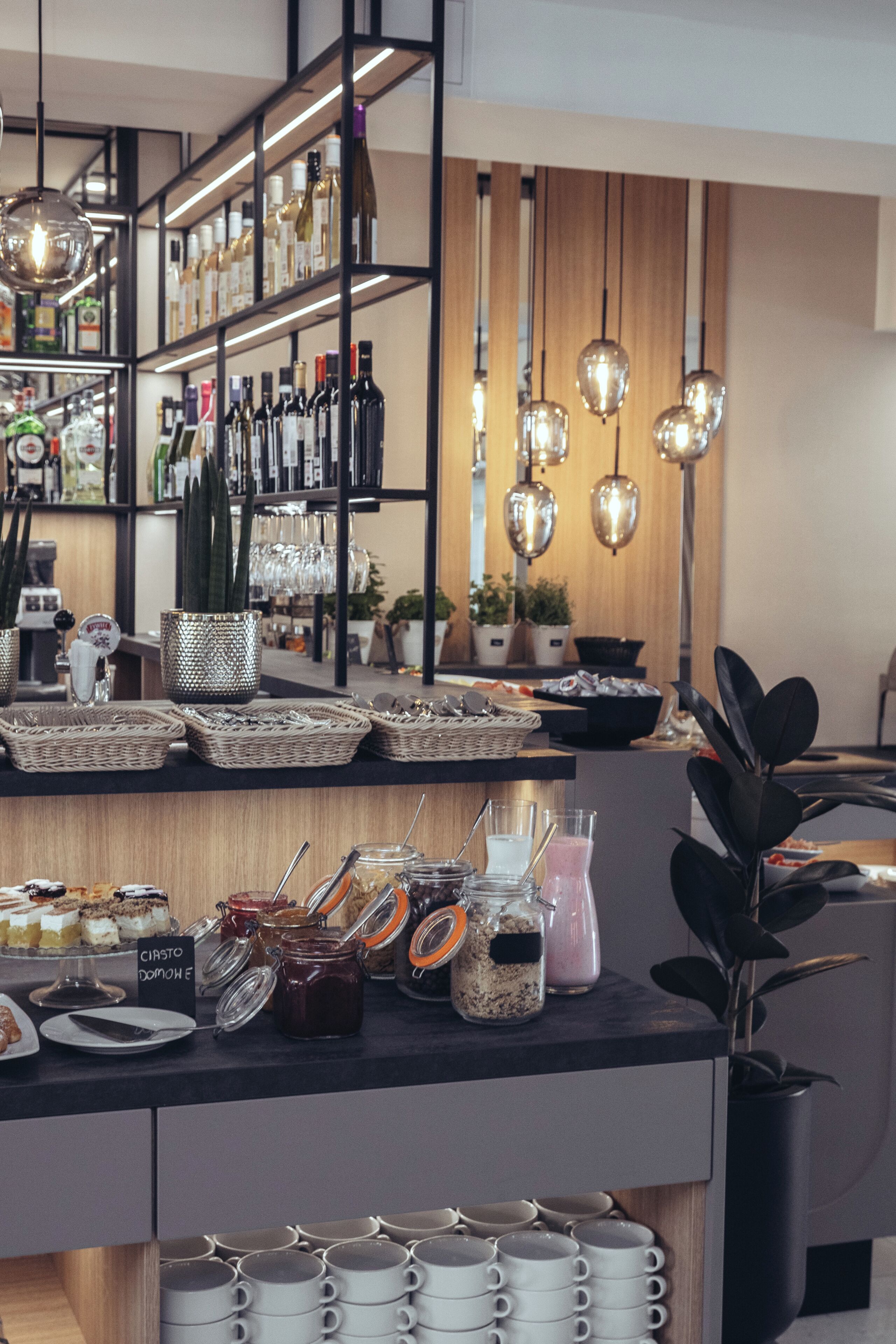 A bar area with shelves of bottles, a counter with food and drinks, and hanging lights.