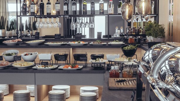 A modern bar area with multiple liquor bottles, glasses, and a buffet setup. - Hotel Fero Express (Kraków)