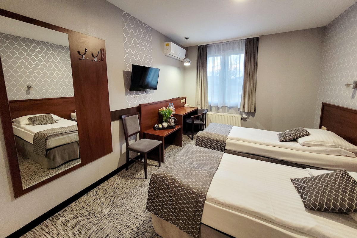 Quarto de hotel com duas camas, uma escrivaninha com cadeira, televisão e um espelho grande.