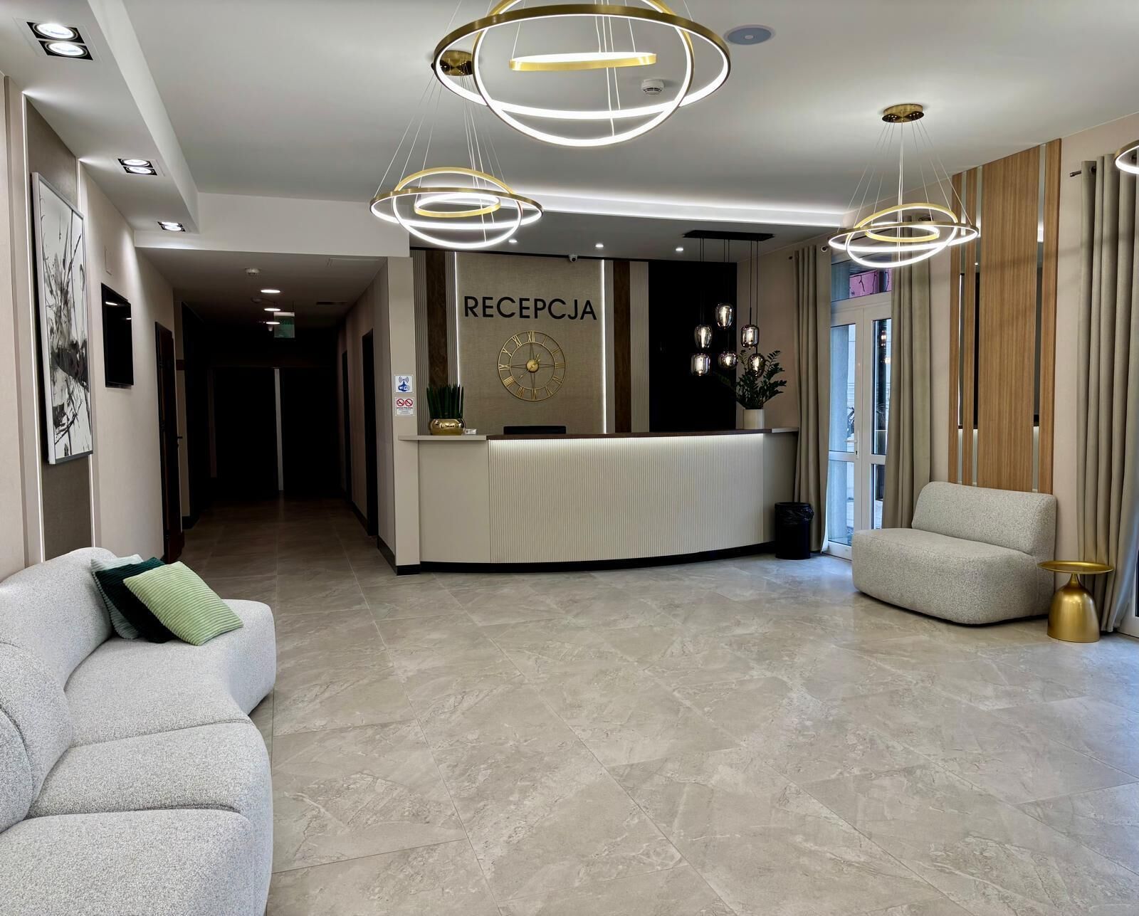 A hotel reception area with a reception desk, a clock, and a seating area with a sofa and armchair.