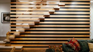 Uma sala de estar moderna com painel de madeira em ripas, uma escada e um sofá verde com almofadas estampadas.