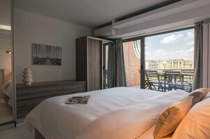 A hotel room with a large bed, a view of the city through a balcony, and a modern design.