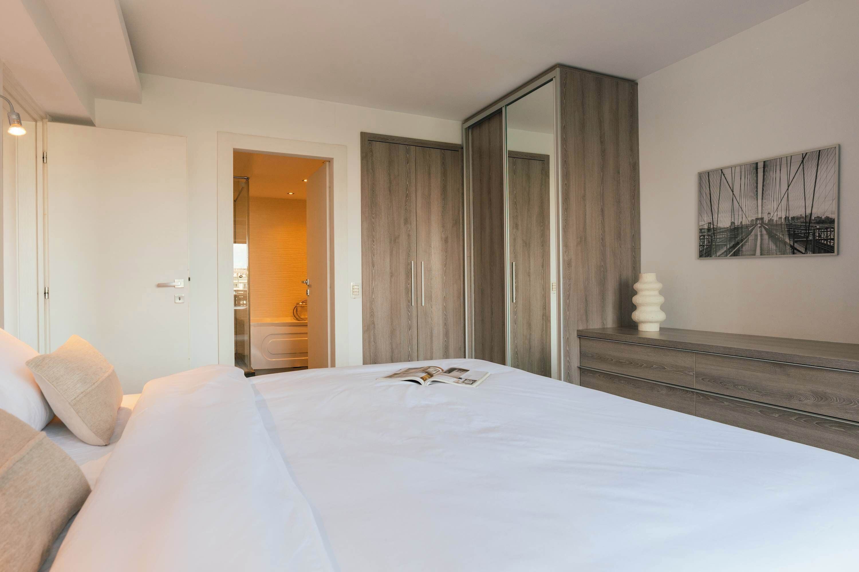 A hotel room with a bed, a wardrobe, a mirror, and a wall-mounted picture.