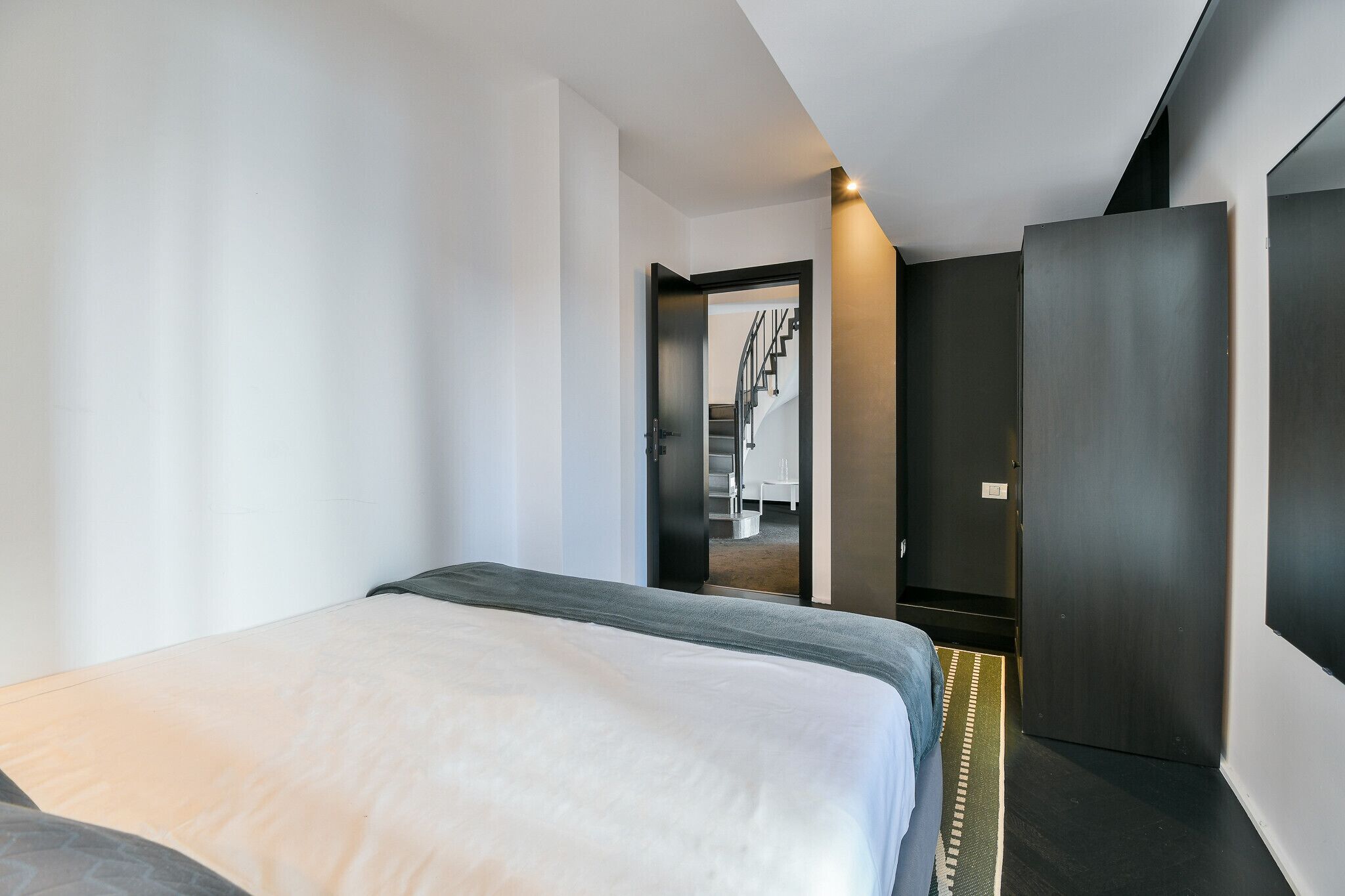 A modern hotel room with a bed, a wardrobe, and a staircase leading to another room.