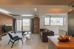 Un apartamento moderno con televisor, sofá, mesa de comedor y un frutero con fruta.