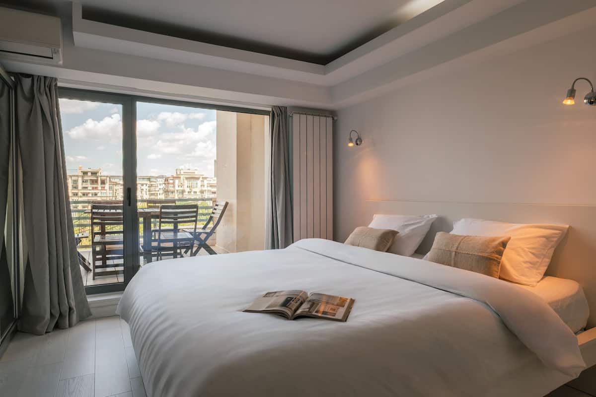 A hotel room with a large bed, a balcony with a table and chairs, and a view of buildings.