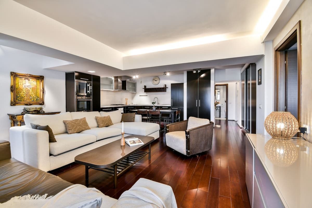 A modern living room with a sofa, armchair, coffee table, and a dining area with a kitchen in the background.