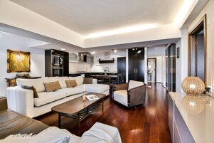 Una sala de estar moderna con sofá, sillón, mesa de centro y un comedor con una cocina al fondo.
