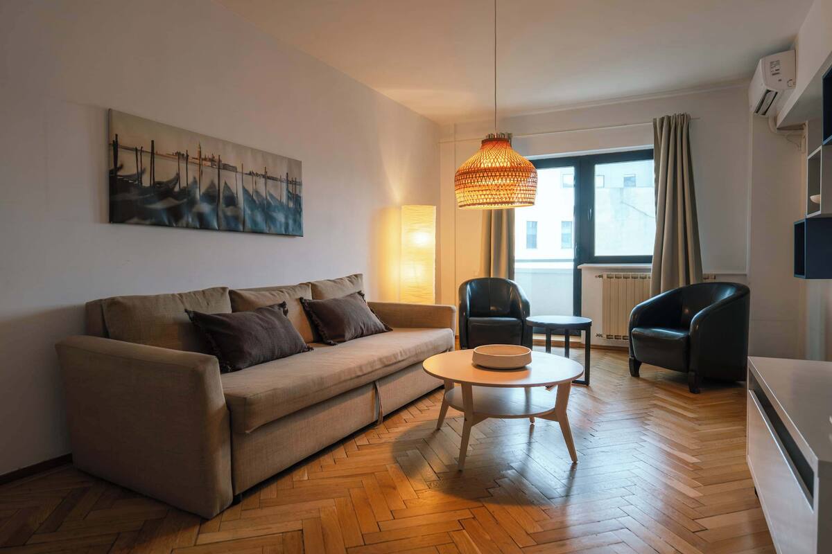 A living room with a sofa, a coffee table, a chair, a hanging light fixture, and a painting on the wall.