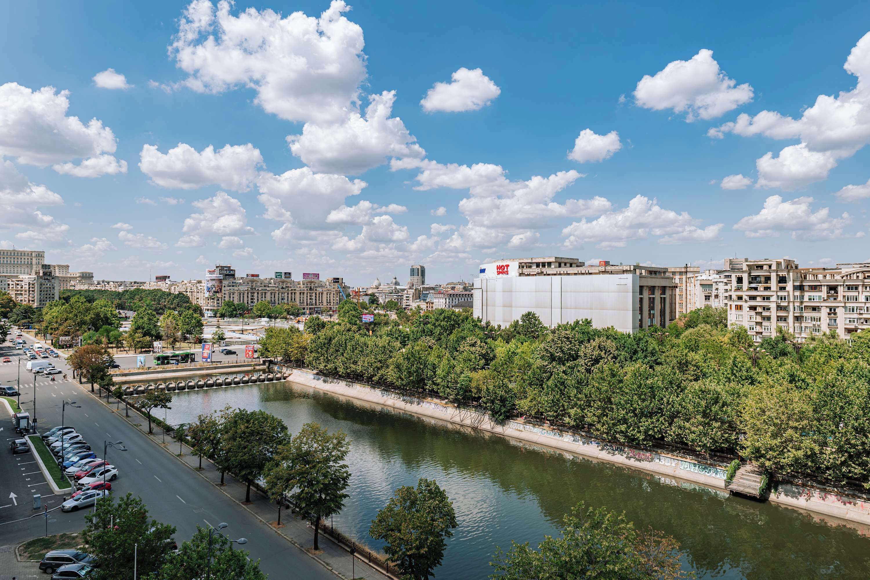 A river with a bridge, a parking lot, and buildings in the background.