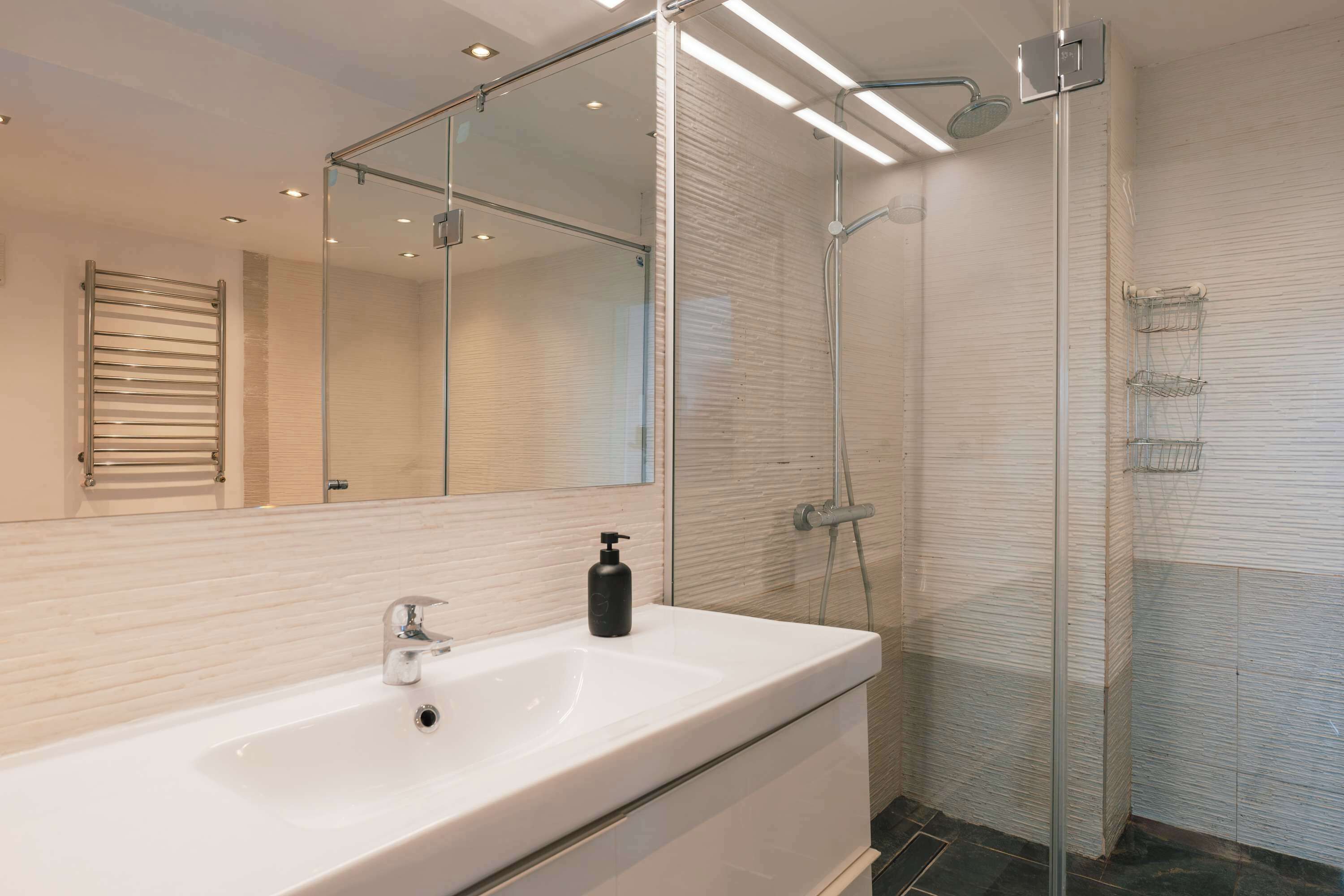 Une salle de bain moderne avec un grand miroir, un lavabo blanc, une douchette à main et une douche à parois de verre.