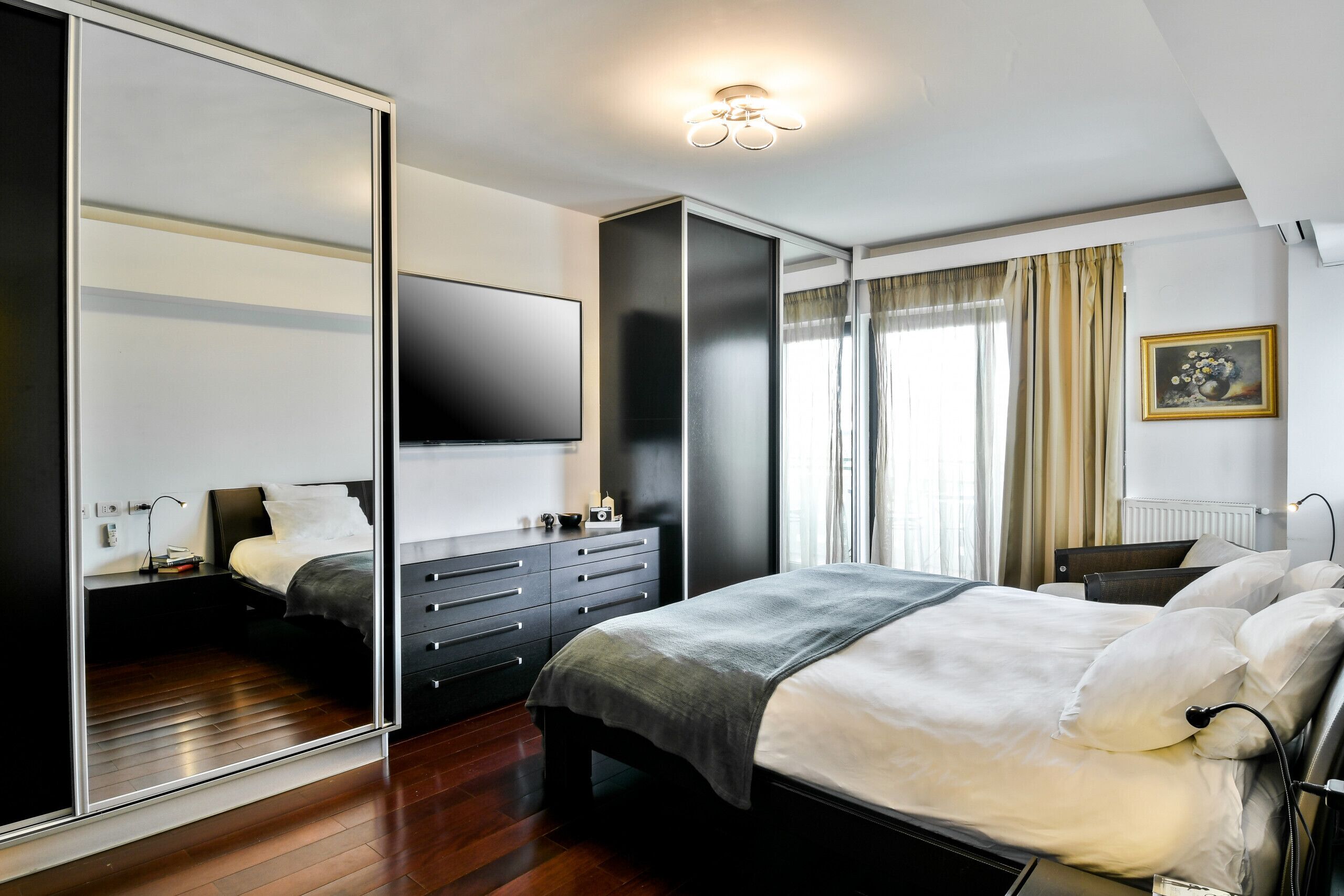 A modern bedroom with a large bed, a wardrobe, a flat-screen TV, and a bedside table.