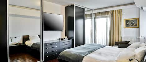 A modern bedroom with a large bed, a wardrobe, a flat-screen TV, and a bedside table.