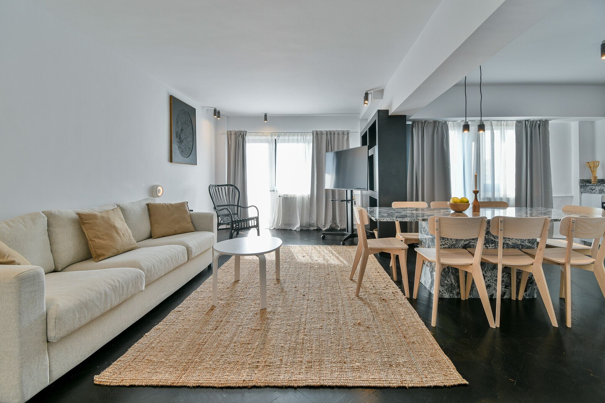 A modern living room with a sofa, a round coffee table, and a dining area with chairs and a table.