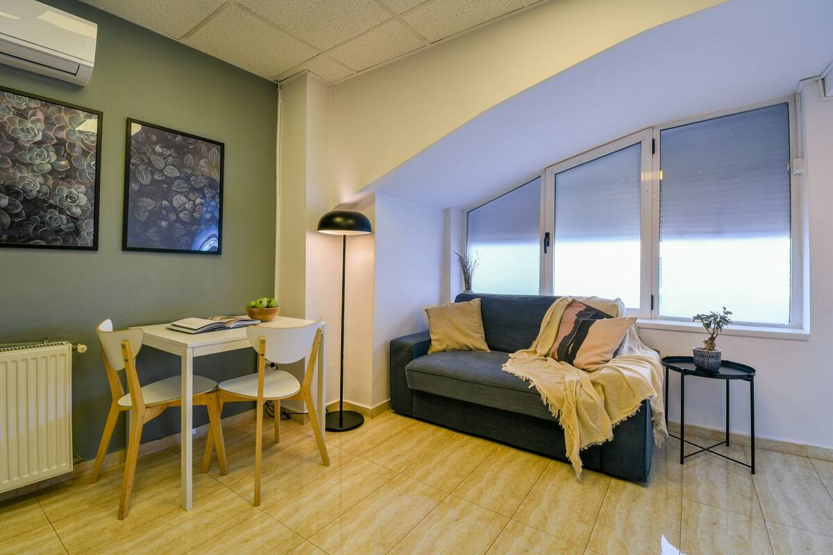 A living room with a sofa, a table, chairs, a floor lamp, and artwork on the wall.