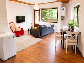 A modern living room with a sofa, a red chair, a TV, a dining table, and a potted plant.