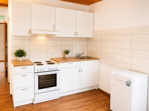A kitchen with white cabinets, a stove, an oven, a sink, and a refrigerator.