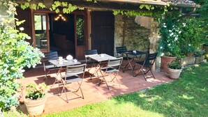 An outdoor patio with tables and chairs, surrounded by potted plants and a stone wall.