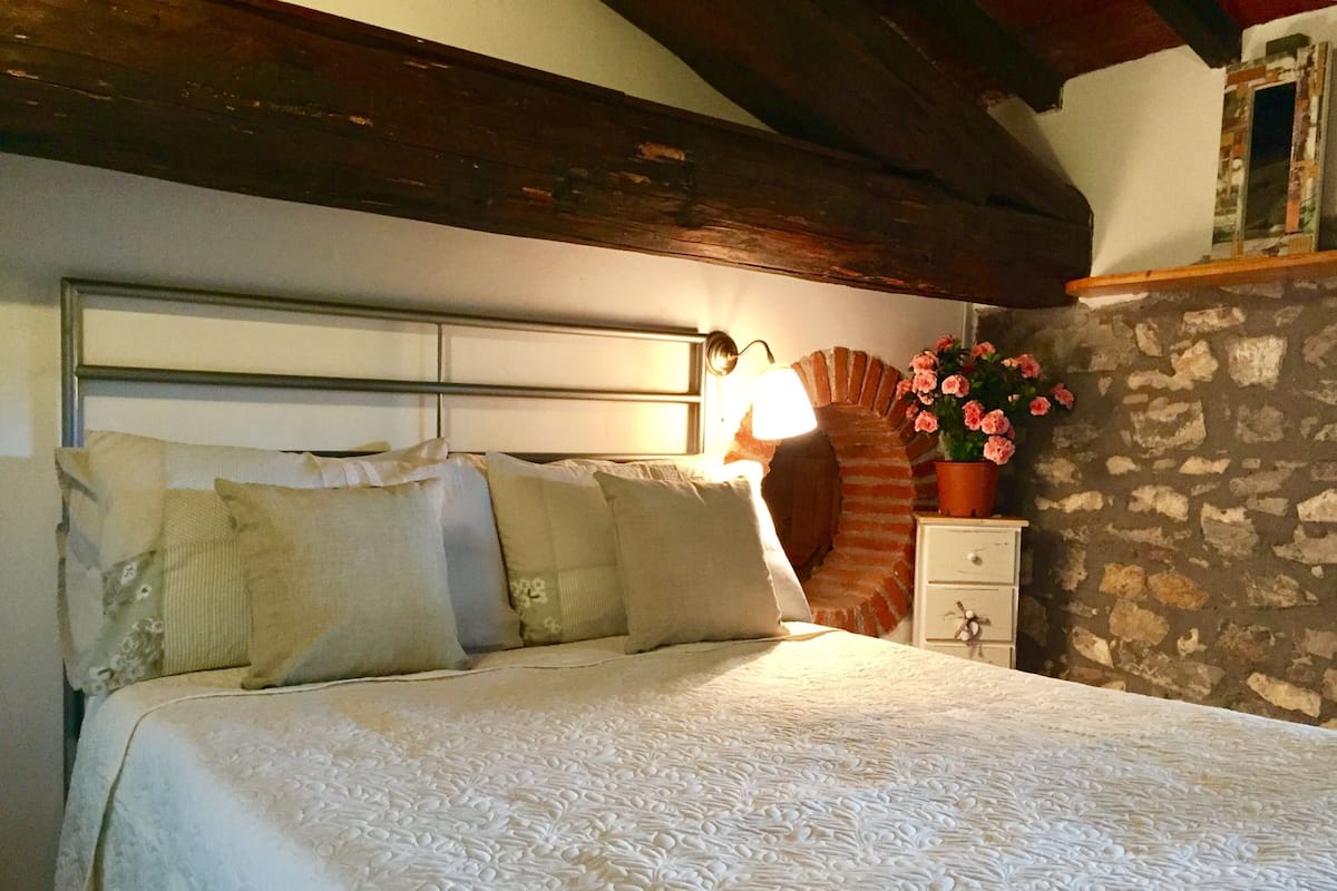 Una cama con colcha blanca, cabecera de madera y mesita de noche con planta en maceta.