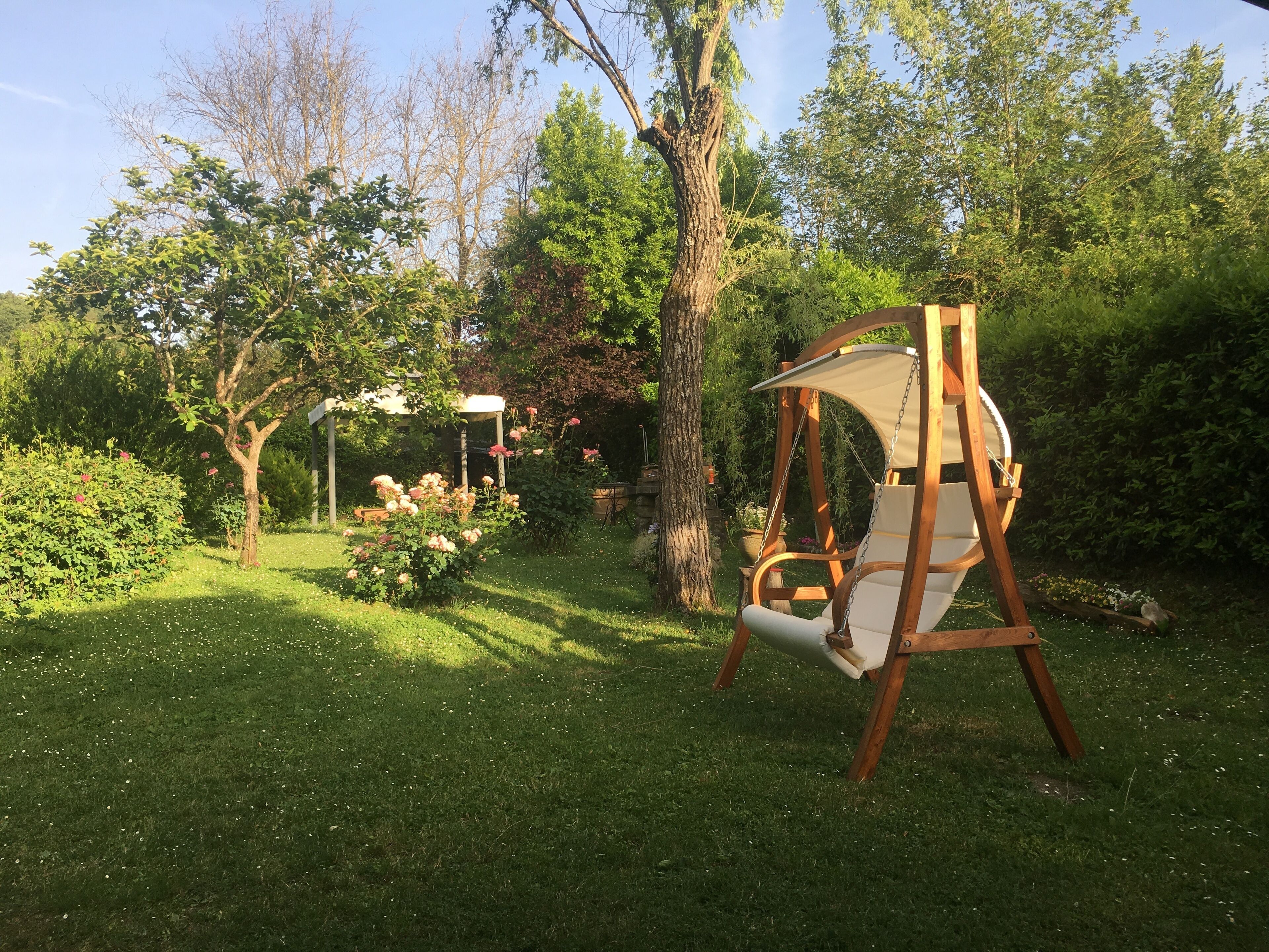 Ein hölzernes Schaukelgestell in einem üppigen Garten mit einer Pergola und blühenden Pflanzen.