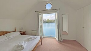 Quarto com cama, mesa de cabeceira, espelho e vista para um lago através de uma porta aberta.
