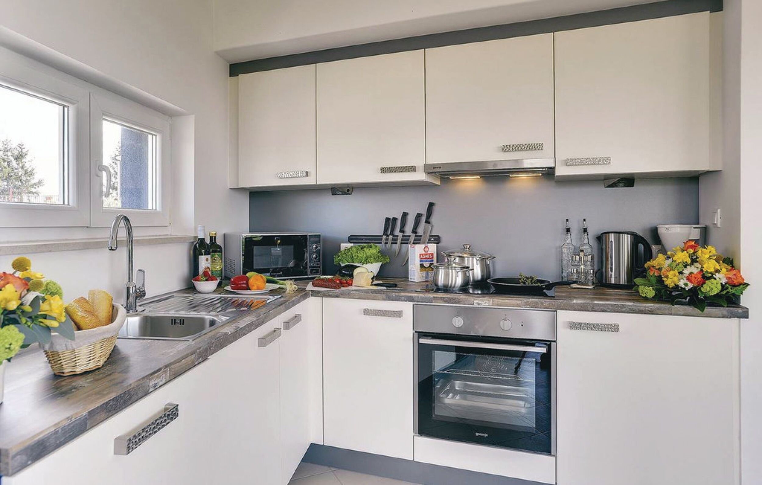 A modern kitchen with white cabinets, a built-in oven, a microwave, and a sink.