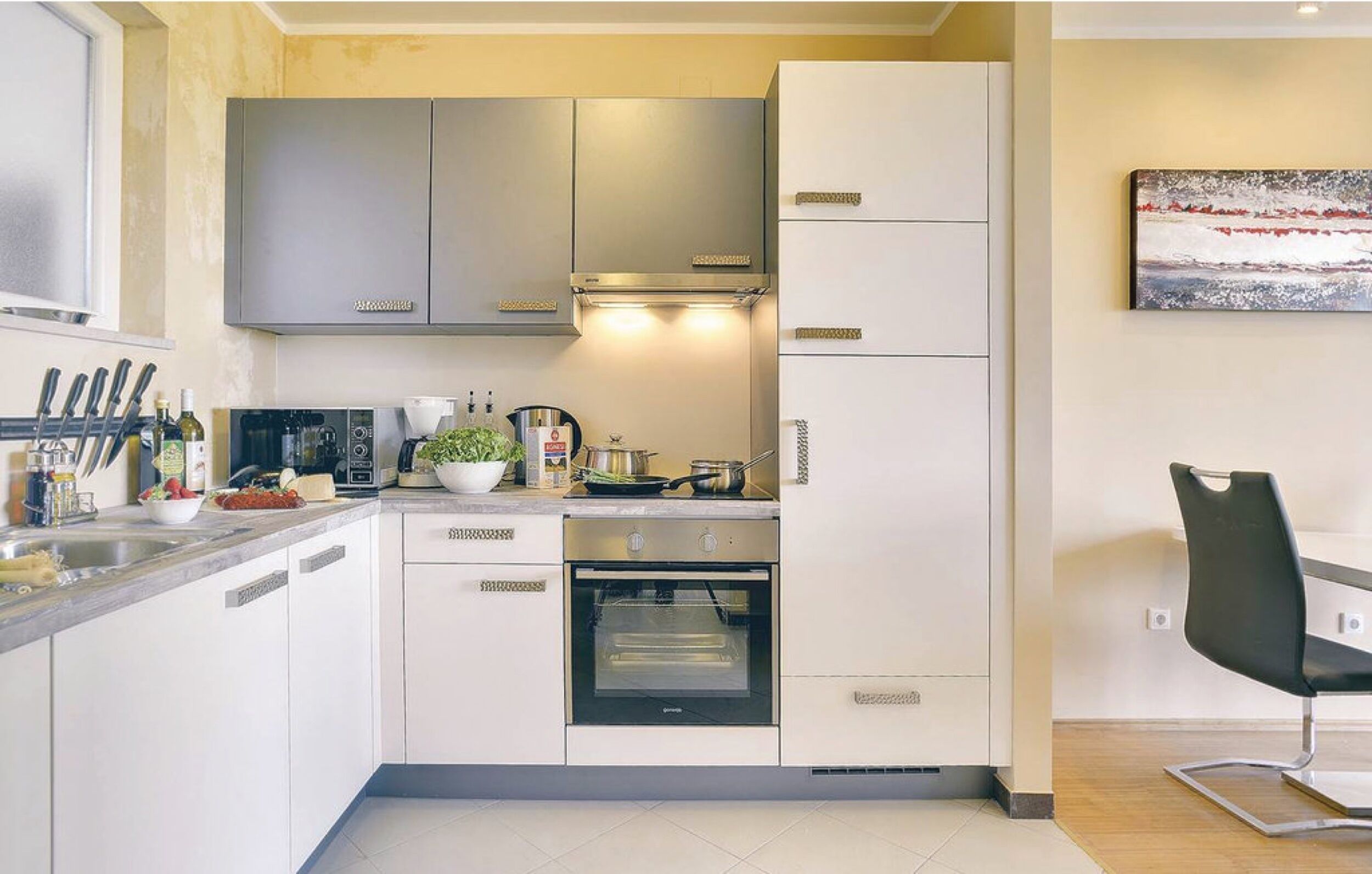 A modern kitchen with white cabinets, stainless steel appliances, and a black chair.