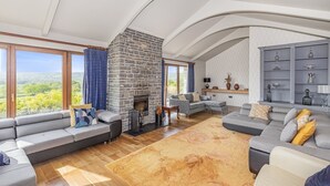 A spacious living room with a stone fireplace, large windows with curtains, and a modern fireplace table. - A large  group retreat that sleeps 16 guests  in 4 bedrooms (Chew Stoke)