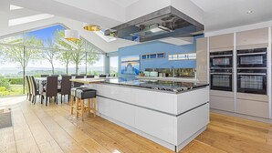 A modern kitchen with a large island, built-in ovens, and a dining area with a view. - A large  group retreat that sleeps 16 guests  in 4 bedrooms (Chew Stoke)
