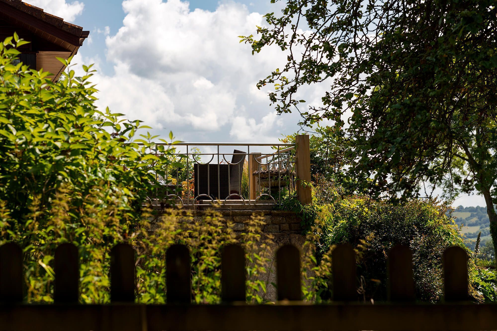 Vista di un giardino con un cancello in metallo, un muro in pietra e un edificio sullo sfondo.
