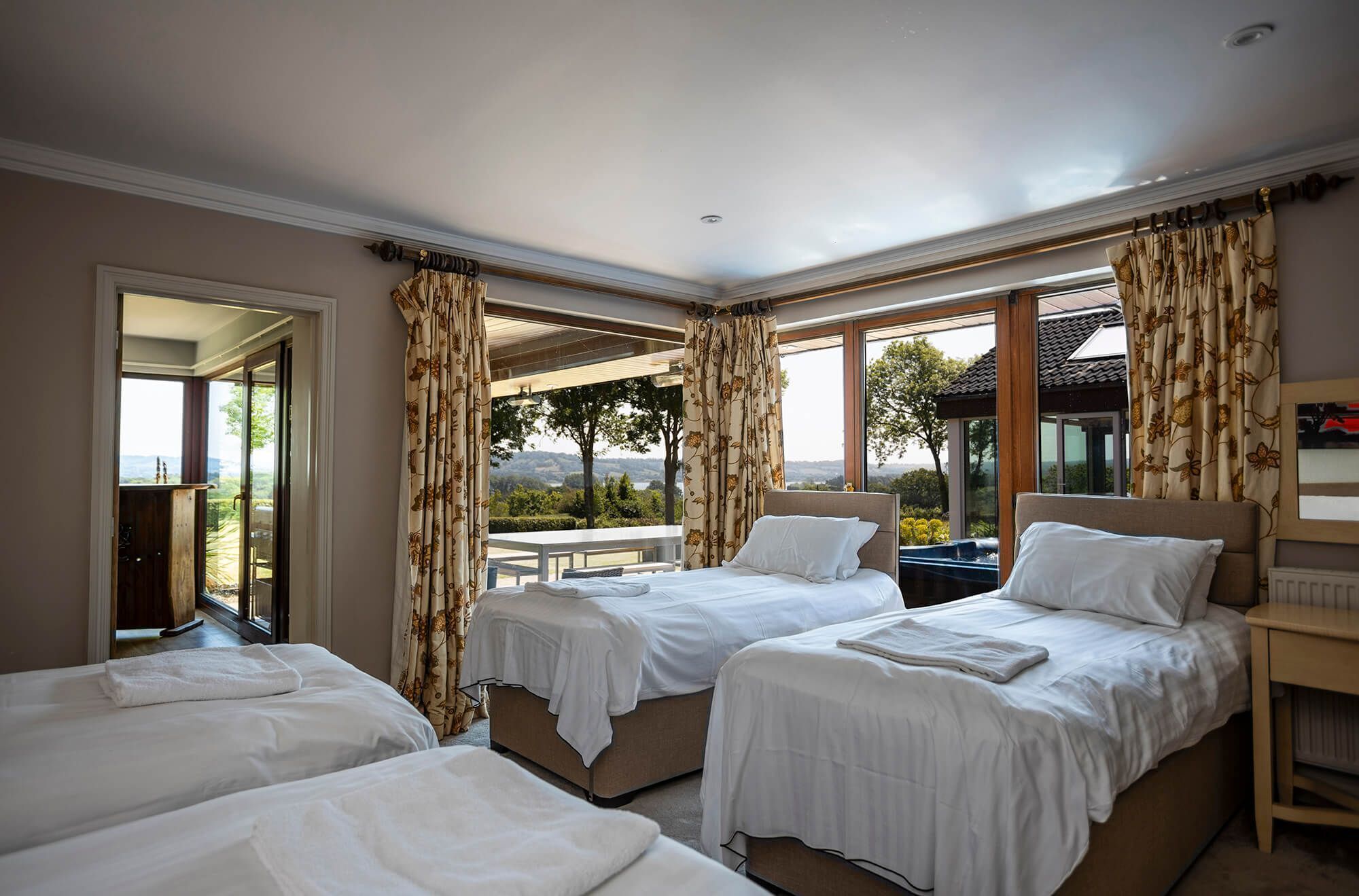 Une chambre d’hôtel avec trois lits, de grandes fenêtres et une vue sur l’extérieur.