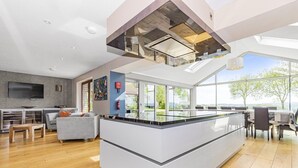 A modern kitchen with a central island, large windows, and a flat-screen TV mounted on the wall. - A large  group retreat that sleeps 16 guests  in 4 bedrooms (Chew Stoke)
