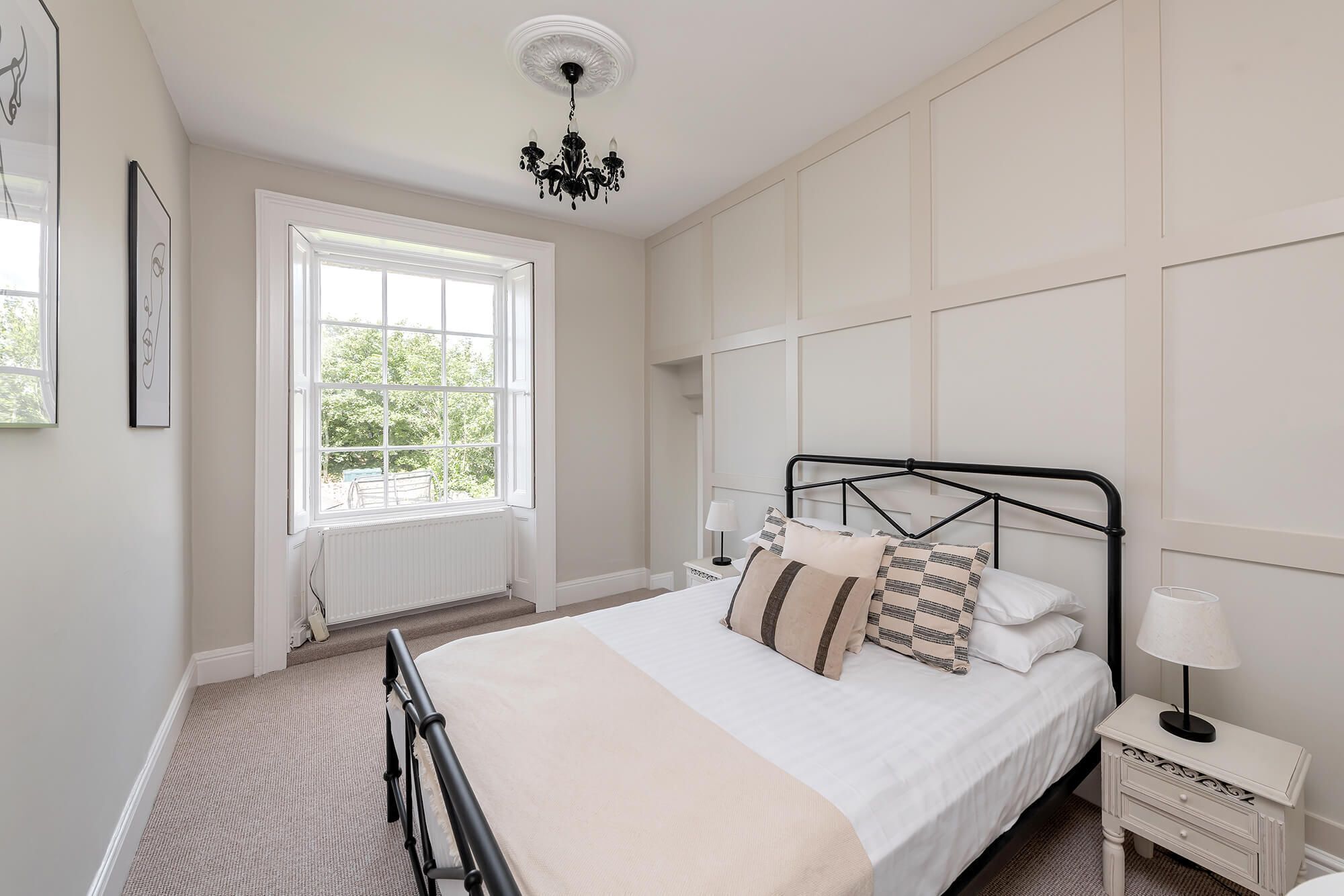 A bedroom with a large bed, a window, a radiator, a nightstand, and a lamp.
