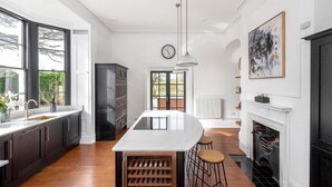 A modern kitchen with a central island, dark cabinetry, and a large window. - Cotswold Manor House - Group Accommodation in The Cotswolds (Badminton)