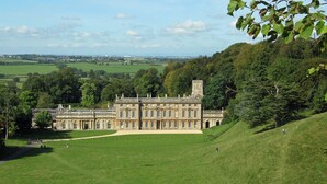 A large, historic building with a symmetrical facade, surrounded by a well-maintained lawn and trees. - Cotswold Manor House - Group Accommodation in The Cotswolds (Badminton)