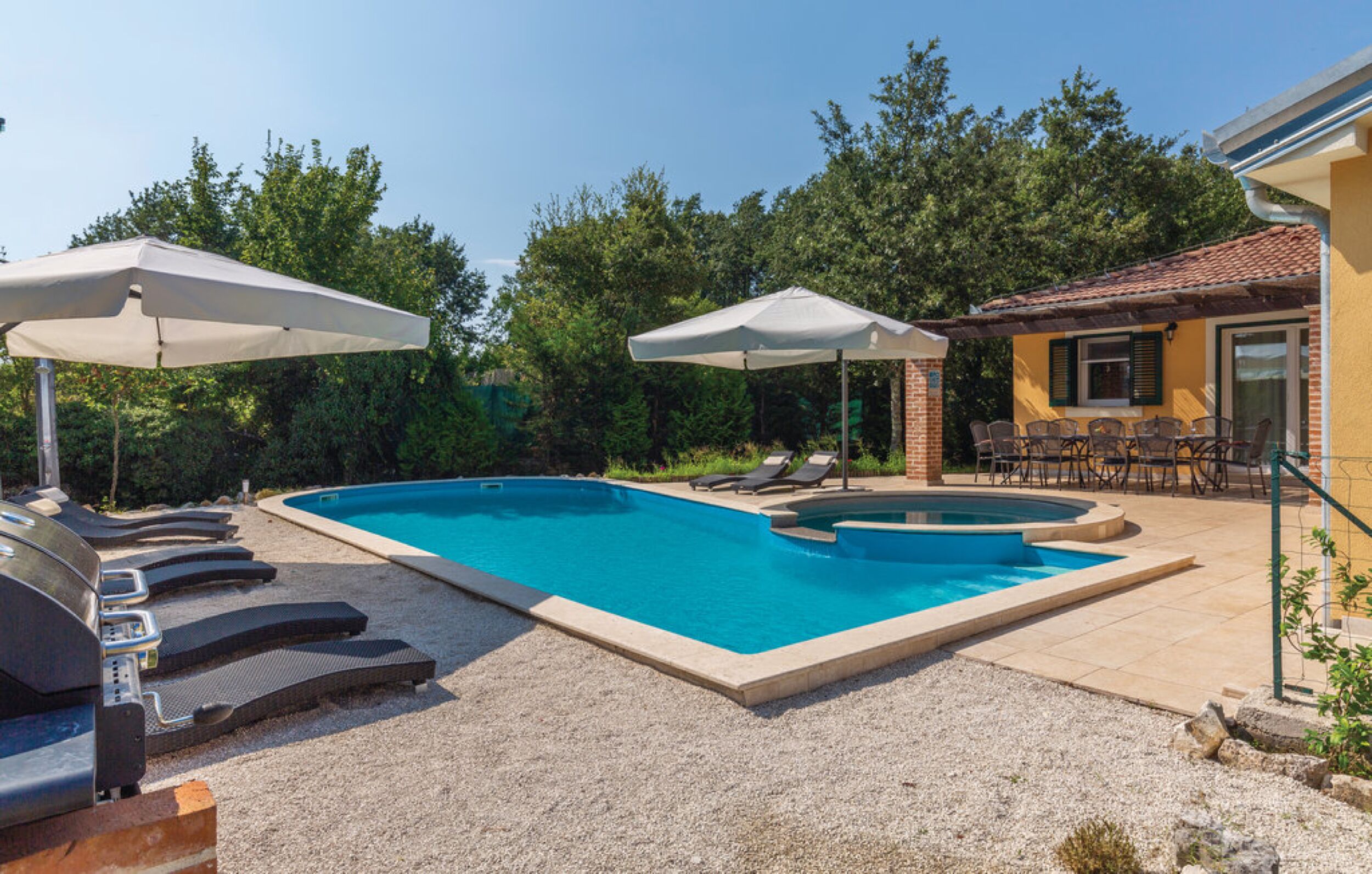 A swimming pool with lounge chairs and umbrellas, surrounded by trees and a building with outdoor seating.