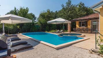 A swimming pool with lounge chairs and umbrellas, surrounded by trees and a building with outdoor seating.
