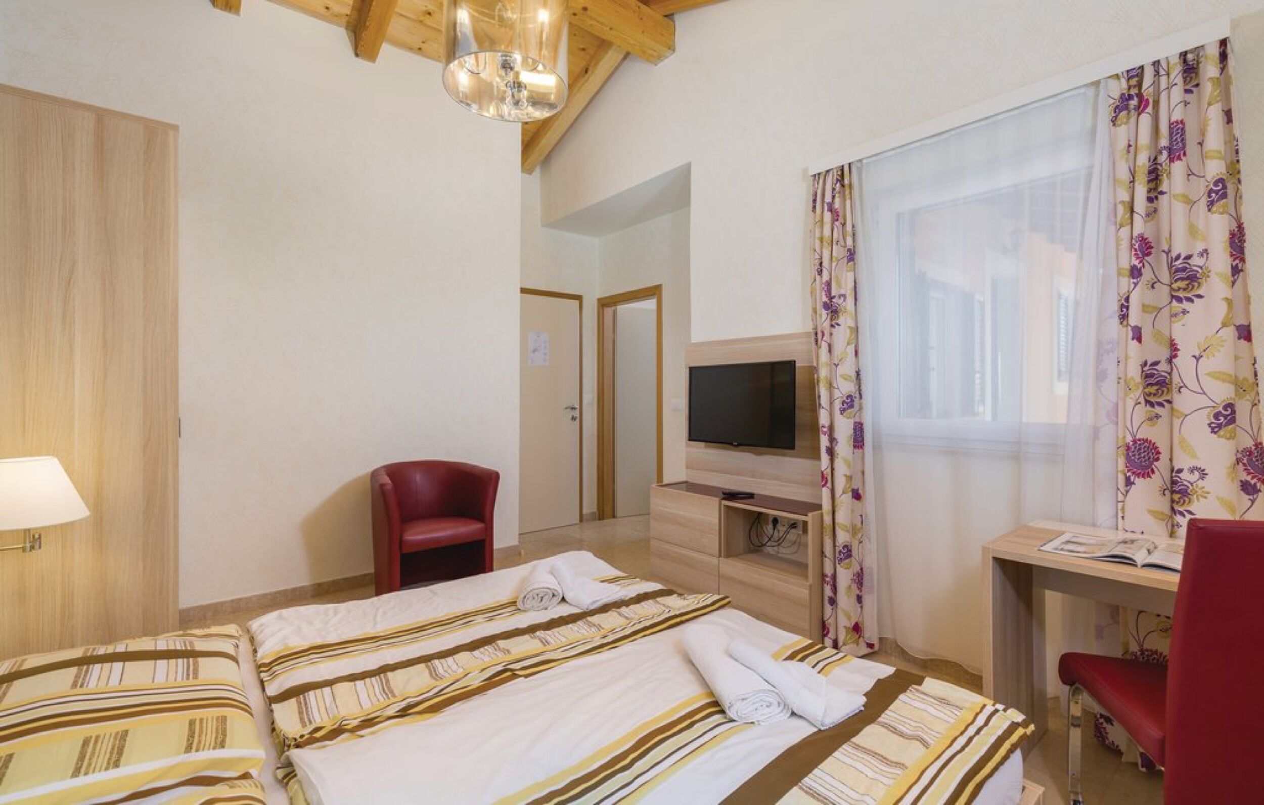 Ein Hotelzimmer mit Bett, Schreibtisch, Fernseher, Stuhl und einem fenster mit Vorhängen.