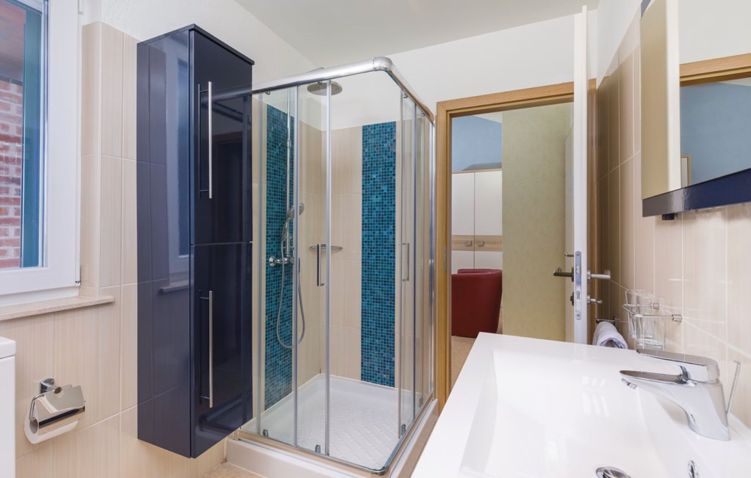 A modern bathroom with a glass shower enclosure, a white sink, and a red chair.