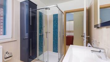 A modern bathroom with a glass shower enclosure, a white sink, and a red chair.