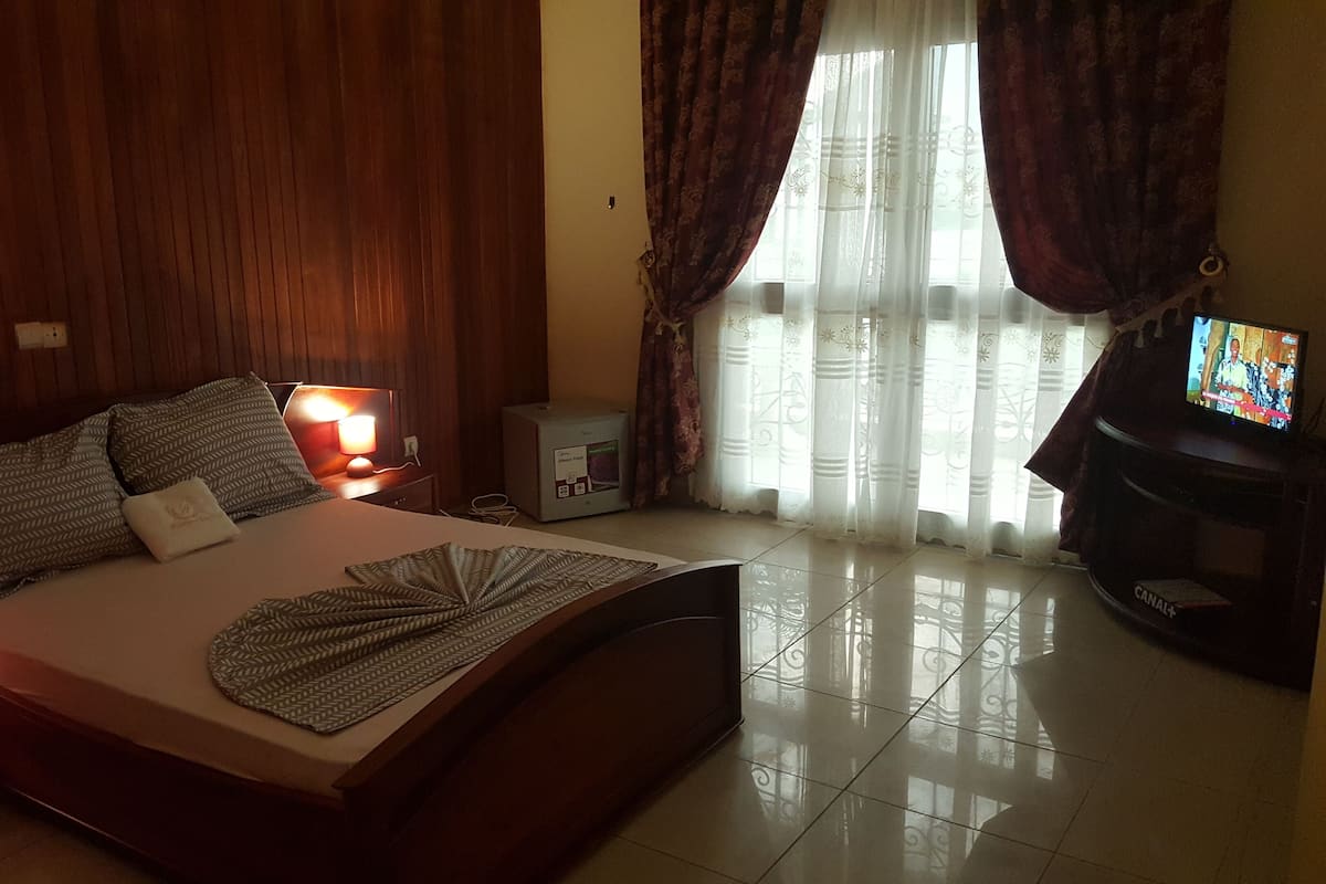 Una habitación de hotel con cama, lámparas de noche, televisor y un refrigerador pequeño.